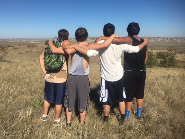 Four kids with arms around each other and looking across the prairie